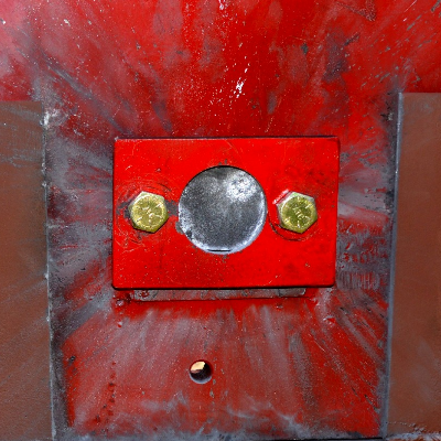 Red painted device where the 50 mm x 50 mm high strenght wear resistant steel plate (AR500) was positioned (in the circle). The image presents the target, positioned 100 meters far from the gun, after the shot and the projectile did not penetrate in the plate, and not even affected the material surface, as will be presented in the other figures.