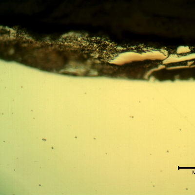 Micrographic detail of the plate section, as polished, close to the surface that suffered the impact.  The deposits at the surface are the melted bullet films.