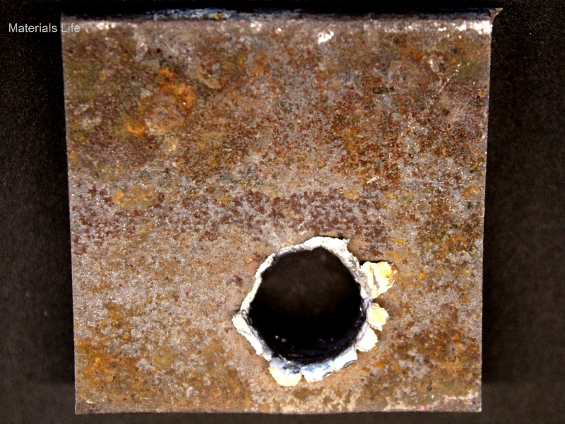 Other view of the 3/8" thickness plate, 50 mm x 50 mm, of the low carbon steel plate, in the face of impact with the projectile. The plate suffered a localized perforation.