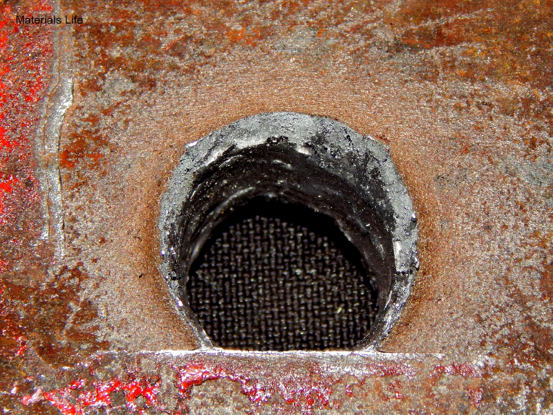 Detail of the position where the projectile exited the plate. The plate suffered a localized perforation and the straight line is marked where the bullet was deviated from the painted device.