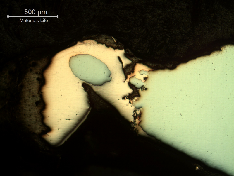 Micrography of the damaged plate at the side of the bullet impact, top of the figure. The perforated hole expulsed the material to the top and bottom directions and the copper alloy is evident at the hole surface.