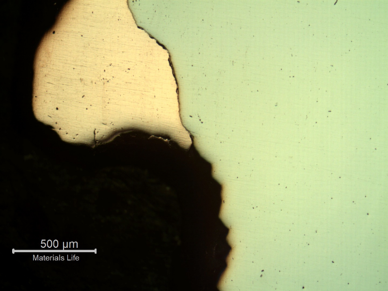 Jagged, torn material boundary at the perforation edge, consistent with localized shear deformation from projectile penetration.