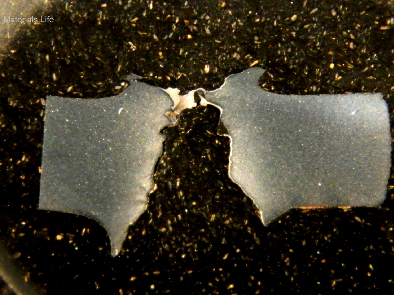 Macrography of the 3/8" thickness low carbon steel plate, in a section. The side of bullet impact is to the top of the figure. The perforated hole expulsed the material to the top and bottom directions. The hole is larger in the exit of the bullet (to the bottom of the figure).