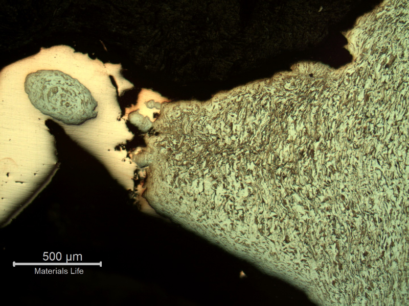 Micrography of the damaged plate at the side of the bullet impact, top of the figure. The perforated hole expulsed the material to the top and bottom directions and the copper alloy is evident at the hole surface.After etching it is clear the strong plastic deformation of the plate microstructure and the hardness level close to the hole increased from 151 HV to 308 HV (1kg).