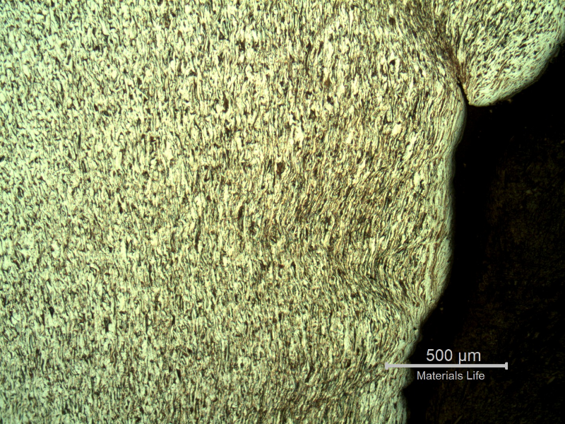 Micrography of the damaged plate at the side of the bullet exit, bottom of the figure. The perforated hole is in the right side of the figure and it is evident a strong plastic deformation of the plate microstructure.  In this region (exit of the bullet) there is no melted film anymore.
