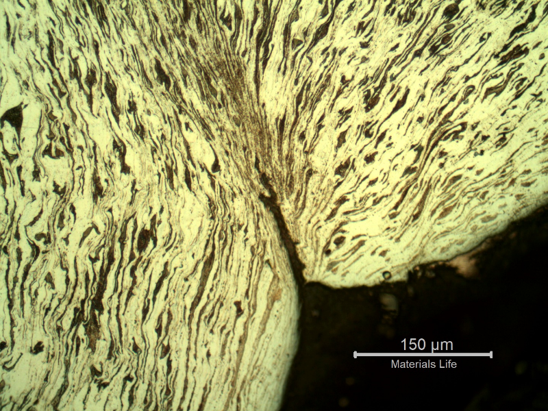 Micrography of the damaged plate at the side of the bullet exit, bottom of the figure. The perforated hole is in the right side of the figure and it is evident a strong plastic deformation of the plate microstructure and several microcracks.  In this region (exit of the bullet) there is no melted film anymore.