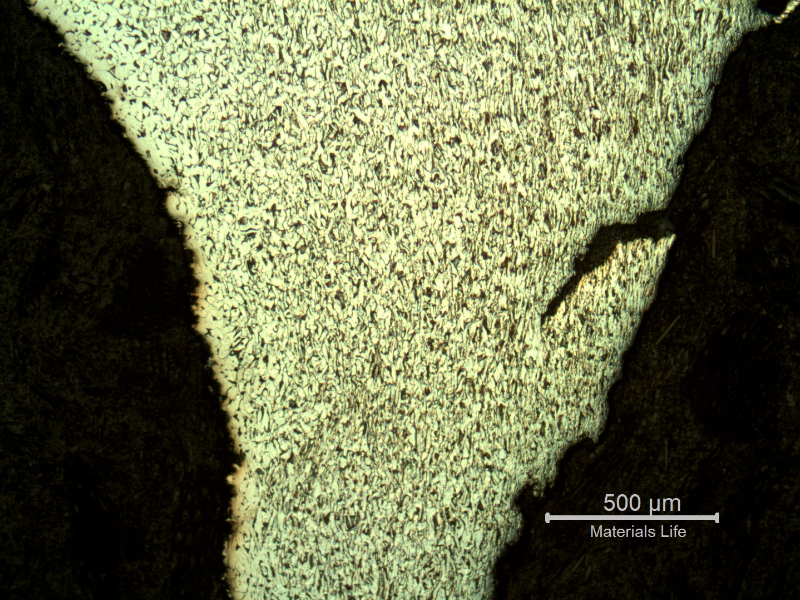 Micrographic detail of the damaged plate at the side of the bullet exit, bottom of the figure. The perforated hole is in the right side of the figure and it is evident a strong plastic deformation of the plate microstructure and microcracks.  In this region (exit of the bullet) there is no melted film anymore.
