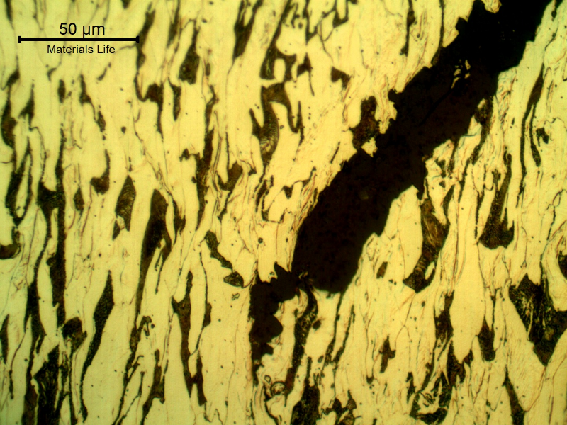 Micrographic detail of the damaged plate at the side of the bullet exit, bottom of the figure. The perforated hole is in the right side of the figure and it is evident a strong plastic deformation of the plate microstructure and microcracks.  In this region (exit of the bullet) there is no melted film anymore.