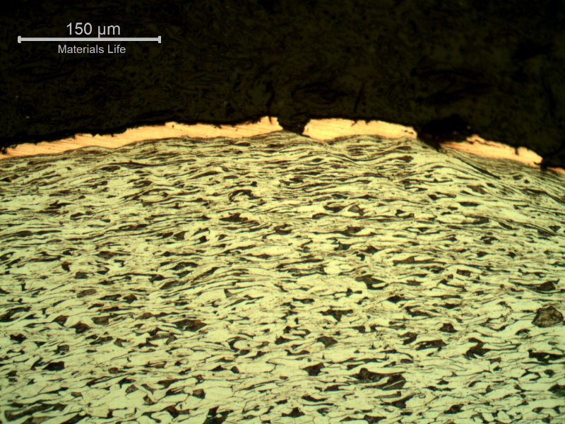 Micrography of the plate section, close to the surface that suffered the impact. The copper alloy melted and created  a yellow-orange deposit. The plate material presented a strong plastic deformation, aligning the grains and strain hardening the microstructure.