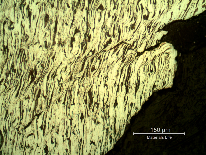 Micrographic detail of the damaged plate at the side of the bullet exit, bottom of the figure. The perforated hole is in the right side of the figure and it is evident a strong plastic deformation of the plate microstructure and microcracks.  In this region (exit of the bullet) there is no melted film anymore.