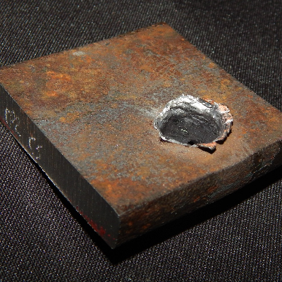 Aspect of the 3/8" thickness plate, 50 mm x 50 mm, of the low carbon steel steel, in the face of impact with the projectile. The plate was perforated by the bullet.