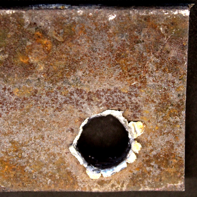 Other view of the 3/8" thickness plate, 50 mm x 50 mm, of the low carbon steel plate, in the face of impact with the projectile. The plate suffered a localized perforation.