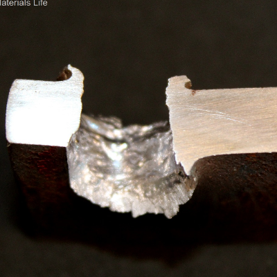 Aspect of the 3/8" thickness plate, 50 mm x 50 mm, of the low carbon steel, in a section transverse to the impact position that is to the top of the figure. The perforated hole expulsed the material to the top and bottom directions. The hole is larger in the exit of the bullet.