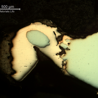 Micrography of the damaged plate at the side of the bullet impact, top of the figure. The perforated hole expulsed the material to the top and bottom directions and the copper alloy is evident at the hole surface.