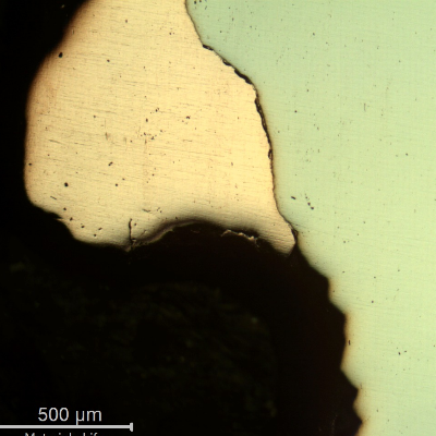 Jagged, torn material boundary at the perforation edge, consistent with localized shear deformation from projectile penetration.