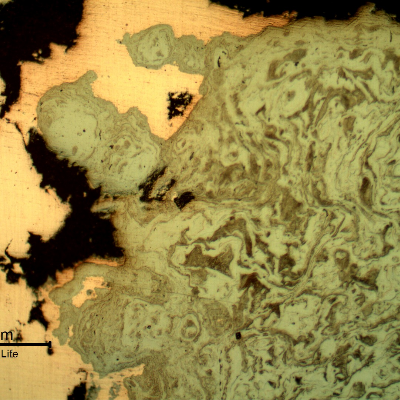 Micrography of the damaged plate at the side of the bullet impact, top of the figure. The perforated hole expulsed the material to the top and bottom directions and the copper alloy is evident at the hole surface.After etching it is clear the strong plastic deformation of the plate microstructure.