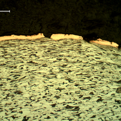 Micrography of the plate section, close to the surface that suffered the impact. The copper alloy melted and created  a yellow-orange deposit. The plate material presented a strong plastic deformation, aligning the grains and strain hardening the microstructure.