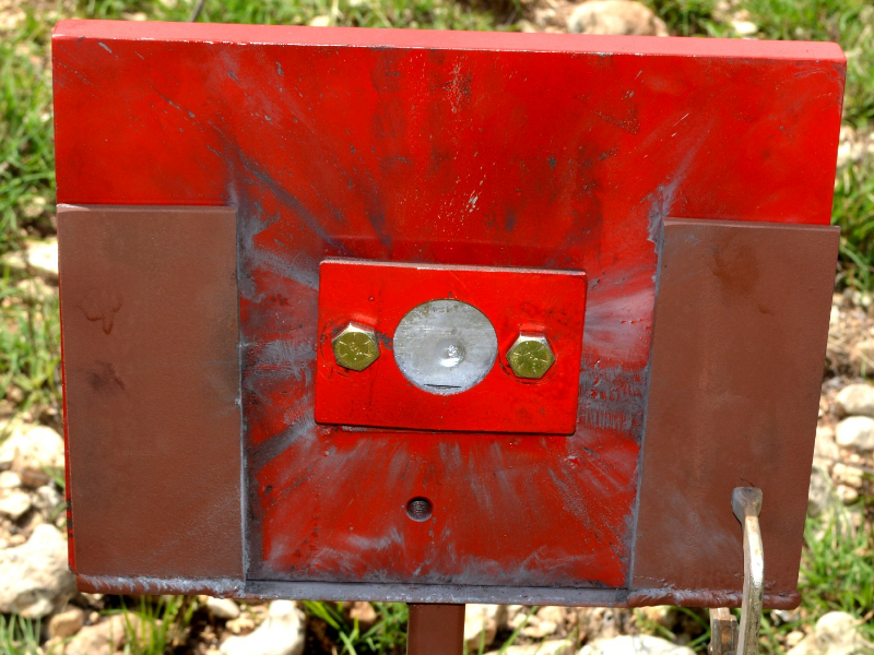 Red painted device where the 50 mm x 50 mm titanium alloy plate was positioned (in the circle). The image presents the target, positioned 100 meters far from the gun, after the shot and the projectile did not perforate the plate, but presented a strong effect, as will be presented in the other figures.