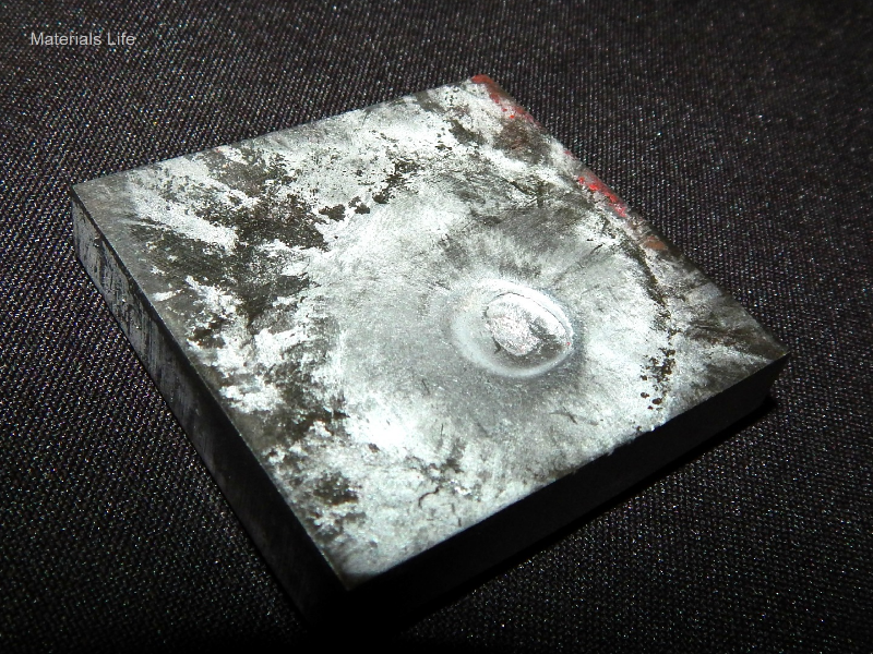 Aspect of the 3/8" thickness plate, 50 mm x 50 mm, of the titanium alloy, in the face of impact with the projectile. The plate was not perforated by the bullet, but suffered localized plastic deformation.
