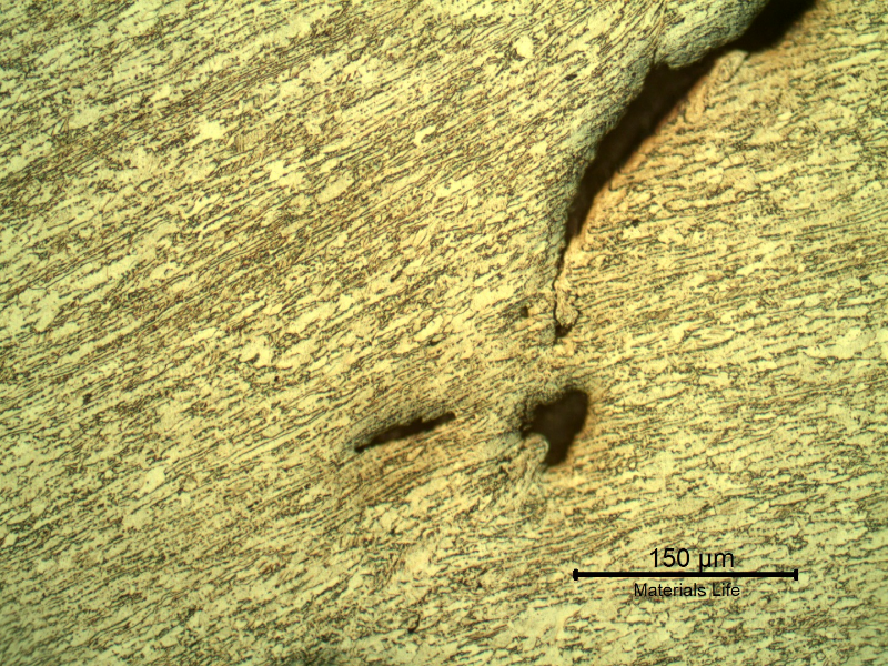 Micrography of the 3/8" thickness titanium alloy plate, in a section. The impact side of the plate is to the top of the figure. The plate was sheared through wall in a very localized position.  HF+HNO3+H2O chemical etch.