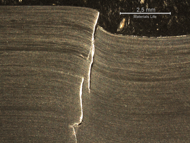 Macrography of the 3/8" thickness titanium alloy plate, in a section. The side of bullet impact is to the top of the figure. The impact sheared the plate wall in a very localized position.  HF+HNO3+H2O chemical etch.
