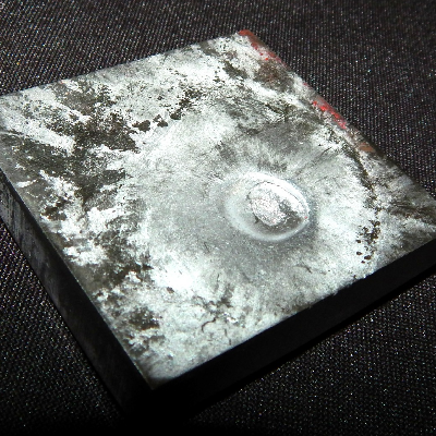 Aspect of the 3/8" thickness plate, 50 mm x 50 mm, of the titanium alloy, in the face of impact with the projectile. The plate was not perforated by the bullet, but suffered localized plastic deformation.
