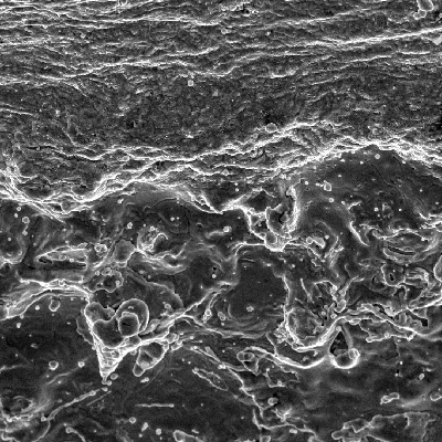 Aspect of the surface of the plate, by scanning electron microscopy, at the margin of the projectile impact position, showing a melted film over the surface.
