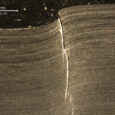 Macrography of the 3/8" thickness titanium alloy plate, in a section. The impact side of the plate is to the top of the figure. The plate was sheared through wall in a very localized position.  HF+HNO3+H2O chemical etch.