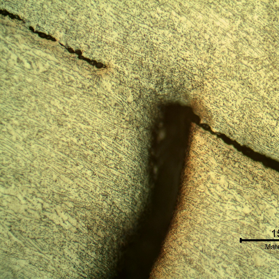 Micrographic detail of the damaged plate (the side of the bullet impact is to the top of the figure). The projectile, in the right side, sheared the plate but did not perforate it and created  longitudinal ductile secondary cracks in the middle of the thickness.  HF+HNO3+H2O chemical etch.