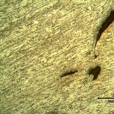 Micrography of the 3/8" thickness titanium alloy plate, in a section. The impact side of the plate is to the top of the figure. The plate was sheared through wall in a very localized position. HF+HNO3+H2O chemical etch.