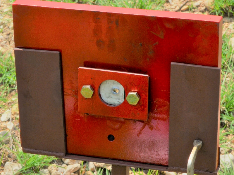 Red painted device where the 50 mm x 50 mm 6061 T6 aluminum alloy plate was positioned (in the circle). The image presents the target, positioned 100 meters far from the gun, after the shot and the projectile perforated the plate.