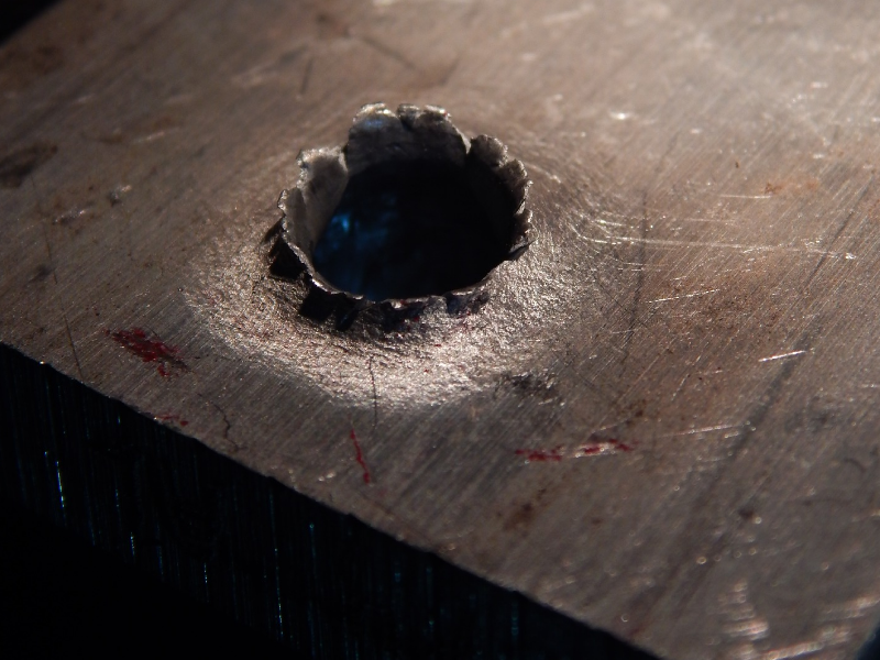 Detail of the margin of the perforated hole in the impact position. It is interesting to observe that the perforation caused the material to be expulsed from the hole, in the direction of the impact.
