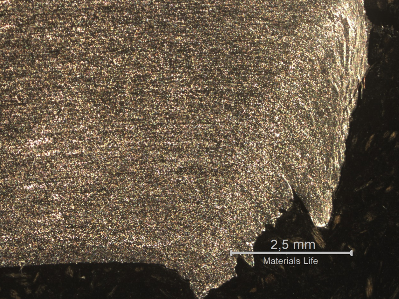 Macrographic detail of the 3/8" thickness aluminum alloy plate. The side of bullet exit is to the bottom of the figure. The perforated hole expulsed the material to the top and bottom directions. The hole is in the right side of the figure