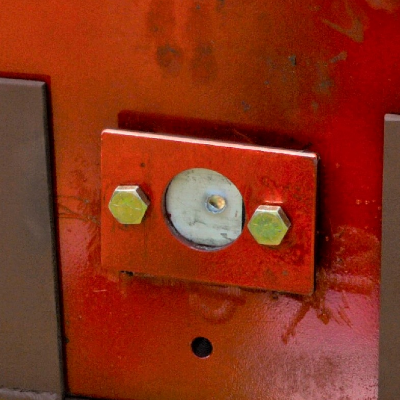 Red painted device where the 50 mm x 50 mm 6061 T6 aluminum alloy plate was positioned (in the circle). The image presents the target, positioned 100 meters far from the gun, after the shot and the projectile perforated the plate.