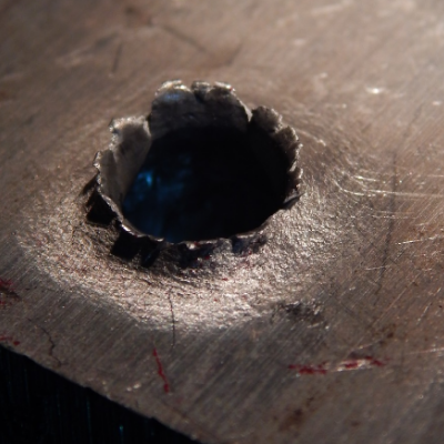 Detail of the margin of the perforated hole in the impact position. It is interesting to observe that the perforation caused the material to be expulsed from the hole, in the direction of the impact.