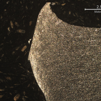 Macrographic detail of the 3/8" aluminum alloy plate. The side of bullet impact is to the top of the figure. The perforated hole expulsed the material to the top and bottom directions. The hole is in the left side of the figure.