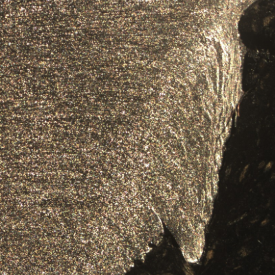 Macrographic detail of the 3/8" thickness aluminum alloy plate. The side of bullet exit is to the bottom of the figure. The perforated hole expulsed the material to the top and bottom directions. The hole is in the right side of the figure