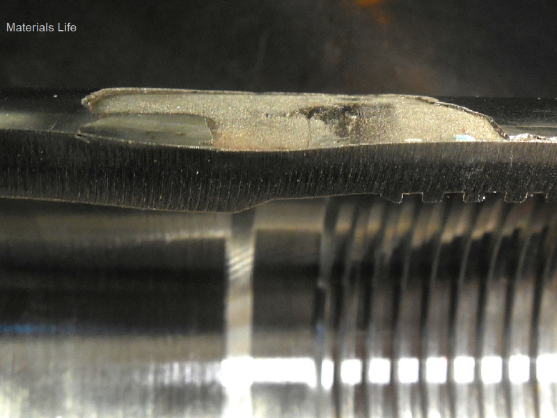 The longitudinal section of the pin at the region of the thermal spray layer detachment, showing that the pin suffered a localized lateral bending with strong plastic deformation, responsible for the layer detachment. The figure shows the external surface (top of the figure) with the layer detachment (gray aspect), the thickness of the pin (deformed) and the internal surface (bright aspect).