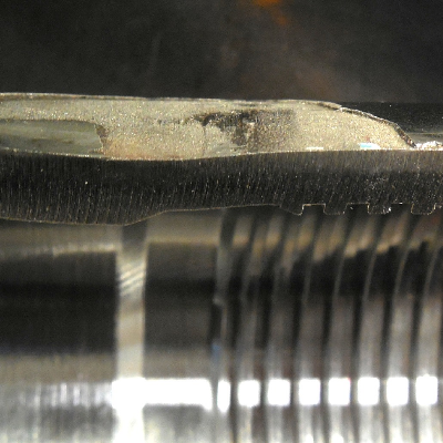 The longitudinal section of the pin at the region of the thermal spray layer detachment, showing that the pin suffered a localized lateral bending with strong plastic deformation, responsible for the layer detachment.  The figure shows the external surface (top of the figure) with the layer detachment (gray aspect), the thickness of the pin (deformed) and the internal surface (bright aspect).