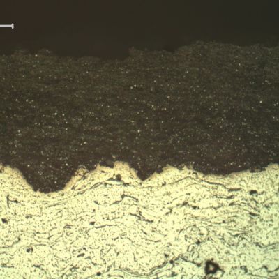 Micrography of a longitudinal section of the sleeve close to the external surface, evidencing a tugnsten carbide thermal spray layer, thickness about 0.2 mm, at the sleeve outer diameter (OD),  black due to the etch (top of the figure). This WC layer was deposited over a stainless steel layer disposed in several layers, non etched.