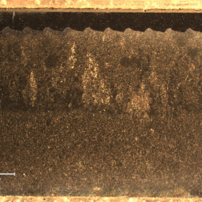 Macrographic aspect of the sleeve longitudinal section where the coating was applied in the external side (top of the figure). It is possible to see that the sleeve was manufactured by centrifugal casting, with  elongated grains from the external side, and equiaxial grains close to the internal side (bottom of the figure). There is a weaved interface between the sleeve and the first layer of thermal spray coating, 1 mm thick; and a second layer of thermal spray coating, 0.2mm thick (almost imperceptible at this low magnification).