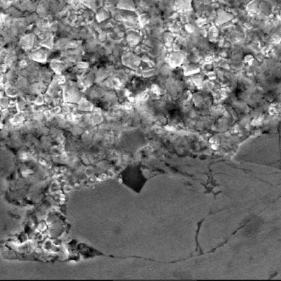 Micrographic detail by scanning electron microscopy of the interface between the two thermal spray layers, the first one in stainless steel (bottom of the figure) and the second one, at the surface,in tungsten carbide (top of the figure). The composition of the first layer is similar to the base metal (lean duplex) and the composition of the second layer is WC in a Co matrix.