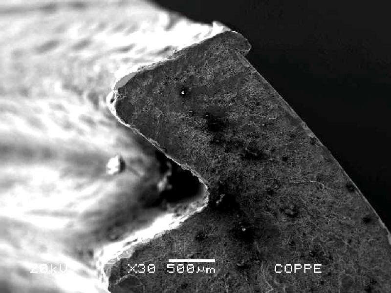 Aspect by scanning electron microscopy of the brittle fracture surface. in a low magnification view. The fracture presents smashed regions (conditions imposed after the fracture was opened) in the region where the chevron marks indicate it is the failure starting point.