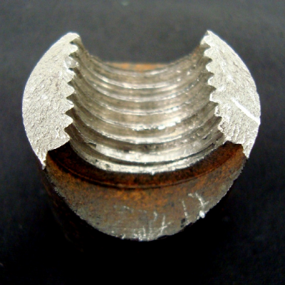 The fracture is flat, in the region of the lower resistant section, presenting no macroscopic evidences of plastic deformation.  The starting point of the fracture is indicated by the chevron marks.