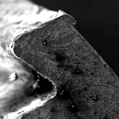 Aspect by scanning electron microscopy of the brittle fracture surface. in a low magnification view.  The fracture presents smashed regions (conditions imposed after the fracture was opened) in the region where the chevron marks indicate it is the failure starting point.