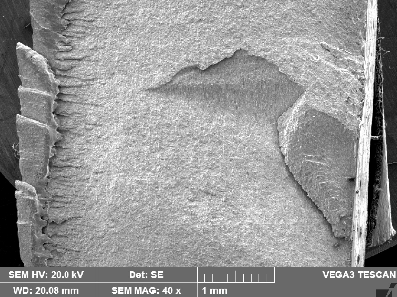 The same fracture appearance of the previous figure, looking at a higher magnification by scanning electron microscopy.  The fracture is clean, flat, starting in the right side of the figure, at the margem of the weld and propagating into the pipe thickness. The external side of the pipe is to the right side of the figure and the internal side of the pipe is to the left side of the figure.