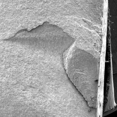 The same fracture appearance of the previous figure, looking at a higher magnification by scanning electron microscopy.  The fracture is clean, flat, starting in the right side of the figure, at the margem of the weld and propagating into the pipe thickness. The external side of the pipe is to the right side of the figure and the internal side of the pipe is to the left side of the figure.