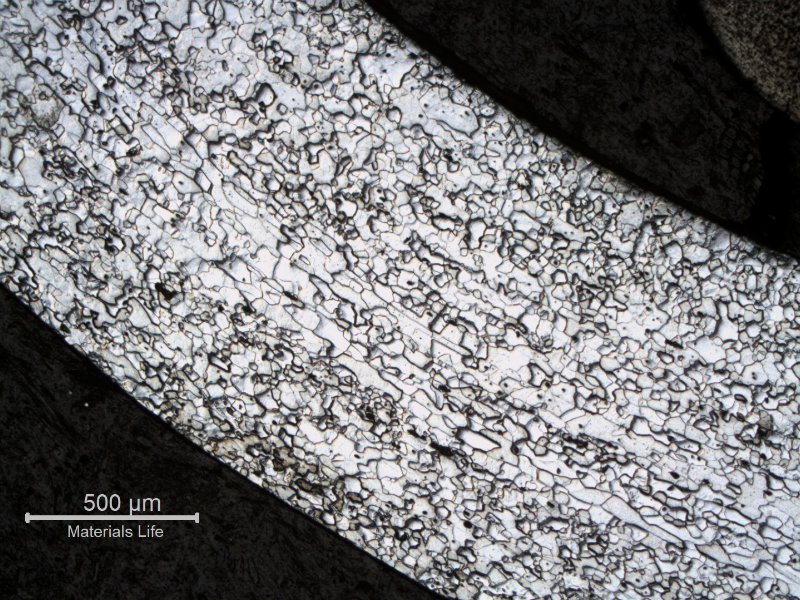 Micrography of the fork handle in the transverse section, curved, presenting differences between grain size and morphology. In the middle section there are elongated grains and close to the surfaces there are smaller  and more equiaxed grains.