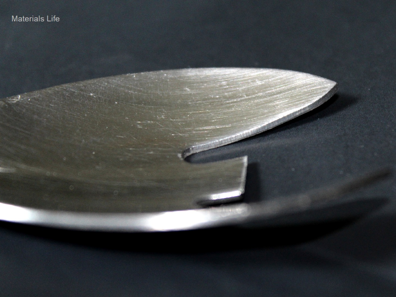 Aspect of the cut surface of the fork tooth in the scoop. The thickness is 1 mm and the fabrication finishing of the surface is polished. The tooth in the center was cut for analysis in the longitudinal section.