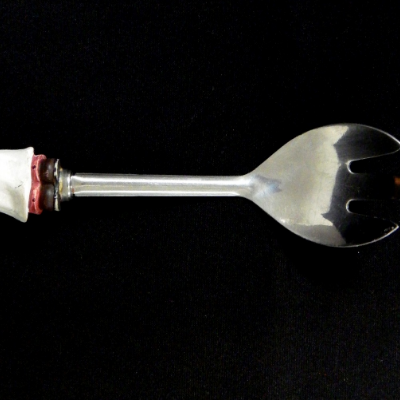 Decorative table service fork, with a non metallic handle that is broken. The metallic part is about 165 mm long and  presents two shapes: the scoop and the handle. The scoop is 53mm wide and 73mm long and the handle is about 9 mm wide and 75 mm long.